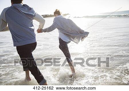 Young couple holding hands and running on beach View Large Photo Image Stock Image - Young couple holding hands and running on beach. Fotosearch