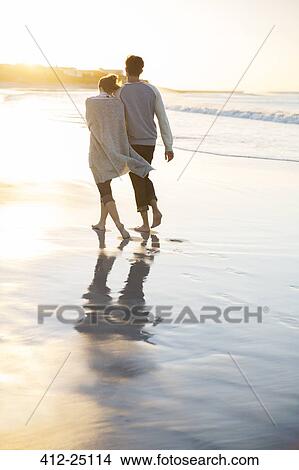 Young couple holding hands and walking on beach at sunset View Large Photo Image Picture - Young couple holding hands and walking on beach at sunset. Fotosearch