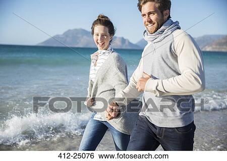 Stock Photograph - Young couple holding hands and walking on beach. Fotosearch