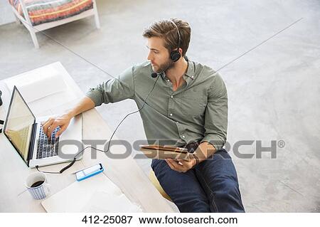 Stock Photo - Young man sitting at desk working with laptop. Fotosearch