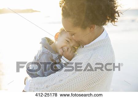 Stock Photo - Young woman embracing daughter on beach. Fotosearch