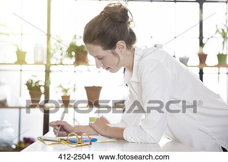 Stock Image - Young woman leaning at desk and writing. Fotosearch
