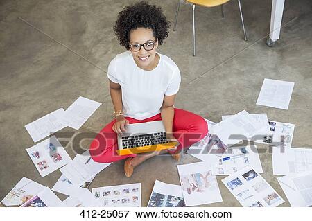 Stock Photo - Young woman sitting on floor and working with laptop. Fotosearch