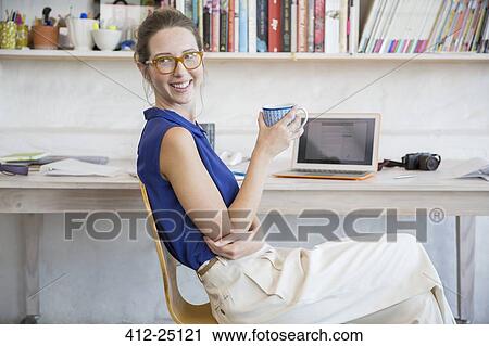 Young woman sitting with mug in home office View Large Photo Image Stock Image - Young woman sitting with mug in home office. Fotosearch