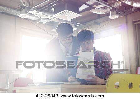 Stock Image - Businessmen reviewing document edits in sunny office. Fotosearch