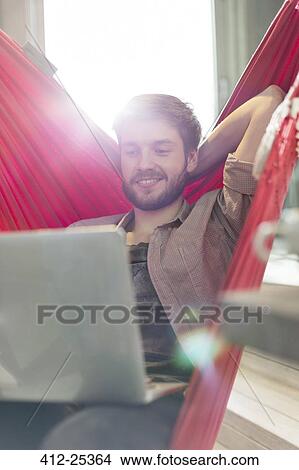 Casual businessman using laptop in hammock in sunny office View Large Photo Image Picture - Casual businessman using laptop in hammock in sunny office. Fotosearch