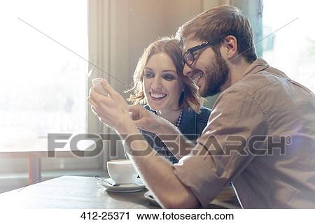 Couple using cell phone in sunny cafe View Large Photo Image Stock Image - Couple using cell phone in sunny cafe. Fotosearch