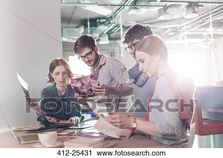 Stock Image - Creative business people reviewing proofs in sunny office. Fotosearch