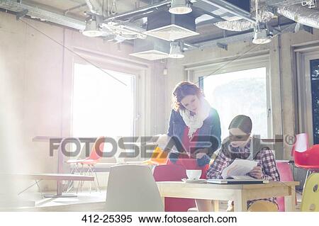 Stock Photography - Creative businesswomen reviewing document edits in sunny office. Fotosearch