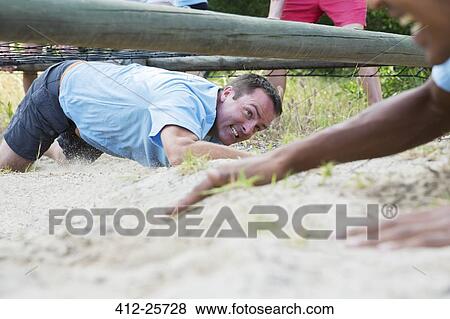 Determined man crawling under net on boot camp obstacle course View Large Photo Image Stock Photo - Determined man crawling under net on boot camp obstacle course. Fotosearch