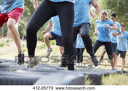 Stock Image - Determined people jumping tires on boot camp obstacle course. Fotosearch