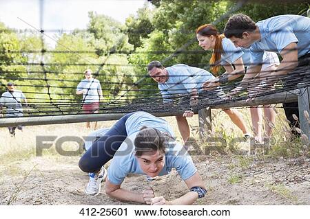 Stock Image - Determined woman crawling under net on boot camp obstacle course. Fotosearch