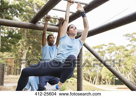 Picture - Determined woman swinging on monkey bars on boot camp obstacle course. Fotosearch