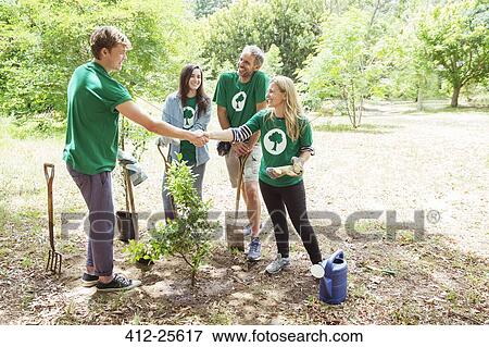Stock Photo - Environmentalist volunteers planting new tree and handshaking. Fotosearch