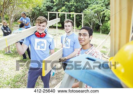 Portrait of smiling volunteers holding planks at construction site View Large Photo Image Stock Image - Portrait of smiling volunteers holding planks at construction site. Fotosearch