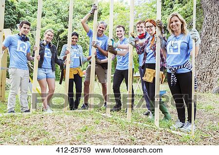 Stock Photo - Portrait of smiling volunteers holding construction frame at construction site. Fotosearch