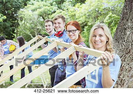 Portrait of smiling volunteers lifting construction frame View Large Photo Image Stock Image - Portrait of smiling volunteers lifting construction frame. Fotosearch