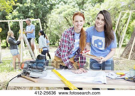 Stock Photograph - Portrait of smiling volunteers with digital tablet and blueprints at construction site. Fotosearch