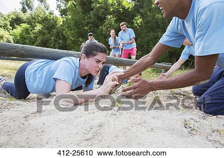 Teammate helping determined woman crawling on boot camp obstacle course View Large Photo Image Stock Image - Teammate helping determined woman crawling on boot camp obstacle course. Fotosearch