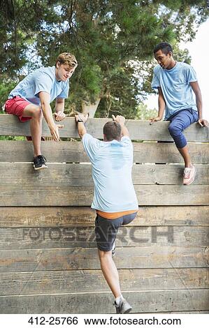Teammates helping man over wall at boot camp obstacle course View Large Photo Image Stock Photograph - Teammates helping man over wall at boot camp obstacle course. Fotosearch