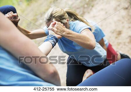 Teammates helping woman climb boot camp obstacle course View Large Photo Image Stock Photography - Teammates helping woman climb boot camp obstacle course. Fotosearch
