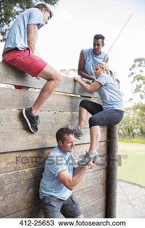 Teammates helping woman over wall on boot camp obstacle course View Large Photo Image Stock Image - Teammates helping woman over wall on boot camp obstacle course. Fotosearch