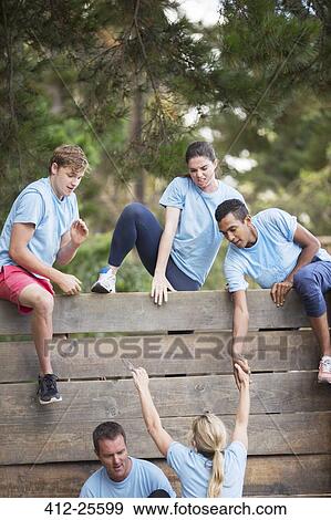 Teammates helping woman over wall on boot camp obstacle course View Large Photo Image Stock Photo - Teammates helping woman over wall on boot camp obstacle course. Fotosearch