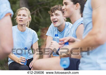Stock Photograph - Tired team resting and drinking water at boot camp. Fotosearch