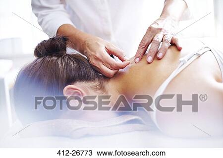 Stock Image - Acupuncturist applying acupuncture needles to woman’s neck. Fotosearch