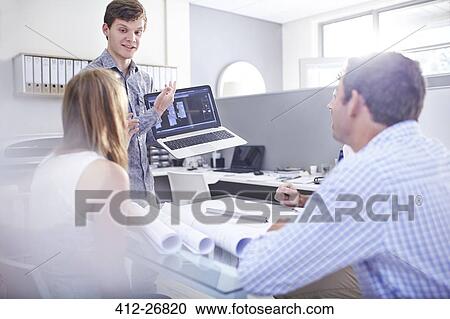 Stock Image - Architects meeting with laptop and blueprints in office. Fotosearch