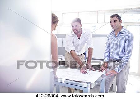 Picture - Architects reviewing blueprints in meeting in office. Fotosearch