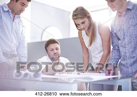 Stock Image - Architects reviewing blueprints in office. Fotosearch