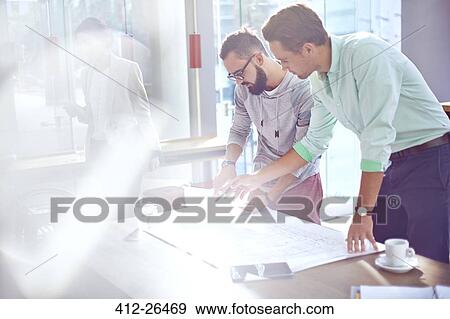 Stock Photo - Architects reviewing blueprints in sunny office. Fotosearch