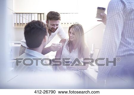 Stock Image - Architects with cell phone drinking coffee in office. Fotosearch