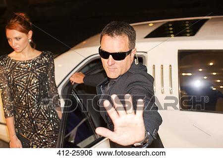 Stock Photograph - Bodyguard protecting celebrity from paparazzi outside limousine at event. Fotosearch