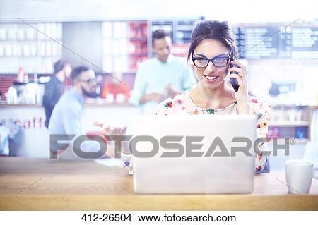 Businesswoman using laptop and talking on cell phone in cafe View Large Photo Image Picture - Businesswoman using laptop and talking on cell phone in cafe. Fotosearch