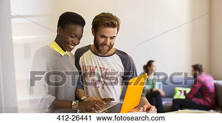 Stock Image - Casual business people sharing laptop in office. Fotosearch
