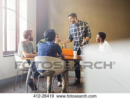 Casual businessman leading meeting at table in office View Large Photo Image Stock Photo - Casual businessman leading meeting at table in office. Fotosearch