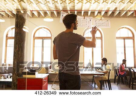 Stock Photo - Casual businessman reviewing hanging diagrams in office. Fotosearch
