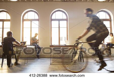 Casual businessman riding bicycle in open office View Large Photo Image Stock Photo - Casual businessman riding bicycle in open office. Fotosearch