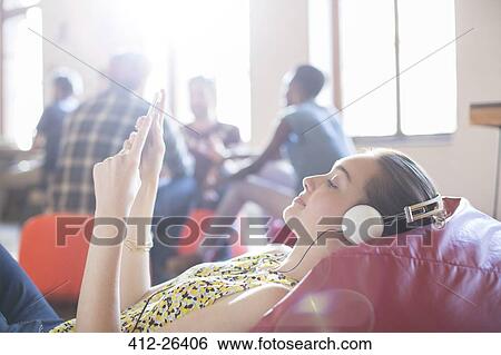 Casual businesswoman relaxing with headphones and digital tablet on bean bag chair View Large Photo Image Stock Photograph - Casual businesswoman relaxing with headphones and digital tablet on bean bag chair. Fotosearch