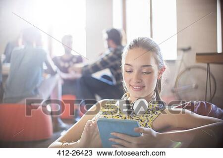 Stock Image - Casual businesswoman with headphones using digital tablet in office. Fotosearch