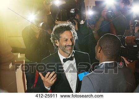 Stock Image - Celebrity being interviewed and photographed by paparazzi photographers at event. Fotosearch