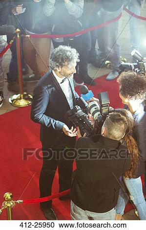 Stock Image - Celebrity being interviewed and photographed by paparazzi photographers at red carpet event. Fotosearch