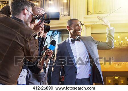 Stock Image - Celebrity waving and being photographed by paparazzi photographers. Fotosearch