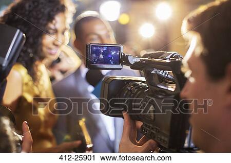 Stock Image - Close up of paparazzi filming celebrity couple at event. Fotosearch