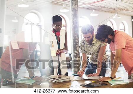 Stock Photo - Creative business people meeting and reviewing proofs in sunny office. Fotosearch