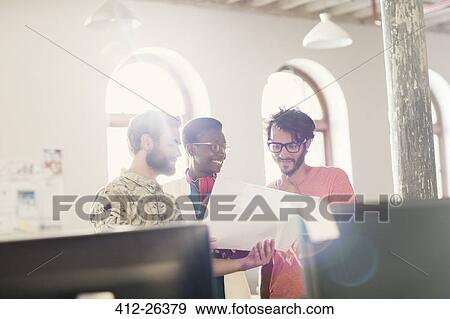 Stock Photo - Creative business people reviewing paperwork in sunny office. Fotosearch