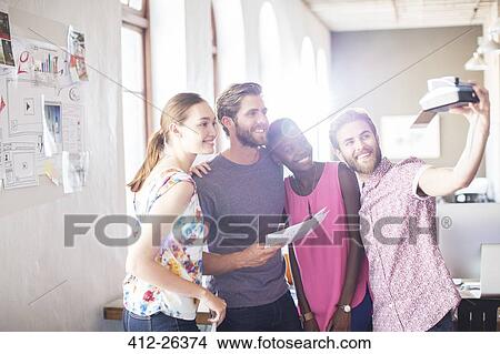 Picture - Creative business people taking selfie with instant camera in office. Fotosearch