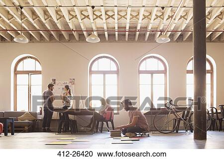 Stock Image - Creative businessman on skateboard working at laptop on floor in open office. Fotosearch